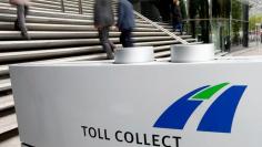 People walk beside a sign at Toll Collect headquarters during a police raid  in Berlin